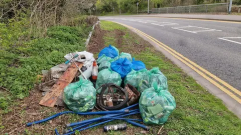 Peterborough Litter Wombles Green plastic bags of litter placed by the side of a road. 