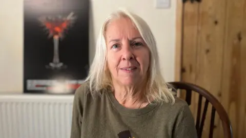 A woman sitting in a chair in front of an anti-spiking campaign poster featuring a cocktail glass with spikes coming out of it.