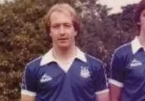 An old photograph of a man with long fair hair wearing a blue and white football strip.