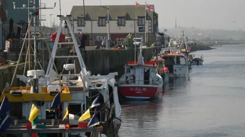 BBC/Shaun Johnson Boats docked at Amble Harbour in Northumberland. The boats float gently on a calm North Sea. 