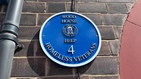 Simon Thake/BBC A round blue plaque on the side of a brick house