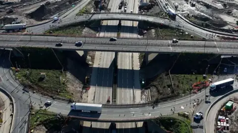 Junction 10 of the M25 seen from above. There are a number of vehicles driving on the roads, and an area of grass in the middle.