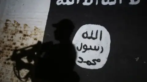 Getty Images A member of the Iraqi forces walks past a mural bearing the logo of the Islamic State (IS) group in a tunnel that was reportedly used as a training centre by the jihadists, on March 1, 2017, in the village of Albu Sayf, on the southern outskirts of Mosul.
