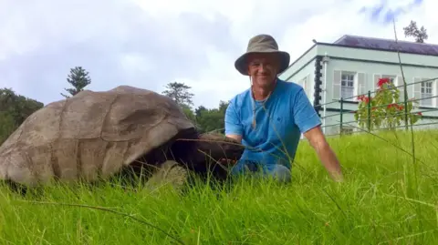 Joe Hollins Joe Hollins, in a blue t-shirt, with the massive tortoise.