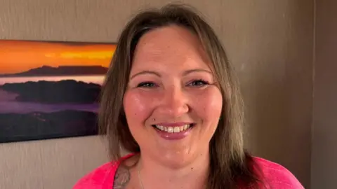 Amy Garcia/BBC Mum Vicky at her home. She has brown hair and smiles at the camera.