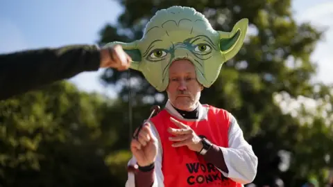 PA Media A man with a short grey beard and a large Yoda hat on his head striking an opponent's conker