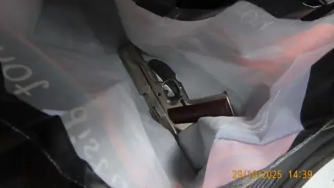 National Crime Agency A silver handgun with a dark handle lying on a piece of crumpled white cloth.