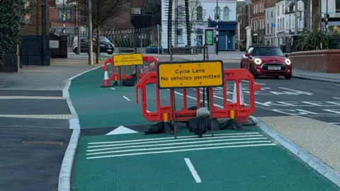 Submitted The cycle Lane in Southgate Street, Gloucester. It is a two-lane green path beside the main road, blocked with orange plastic barriers and road signs saying 'no vehicles permitted'.
