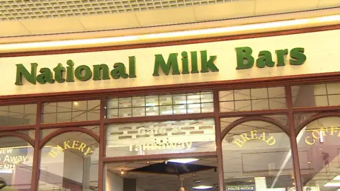 BBC A café sign in green which reads ' National Milk Bars' with a glass frontage with arched windows