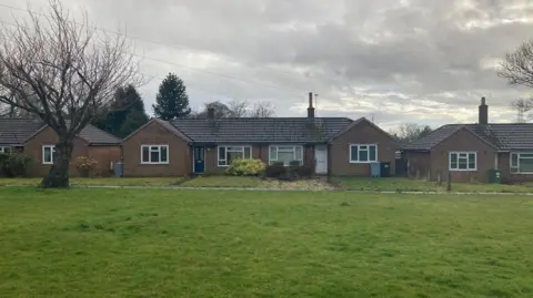 A green space with a bungalow in the background.