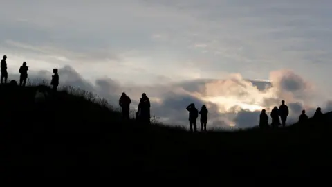 Reuters People look at the sunrise during the celebrations of the Summer Solstice, despite official events being cancelled amid the spread of coronavirus, in Avebury