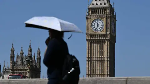 Person walks in front of Big Ben in the heat, carrying an umbrella for shade