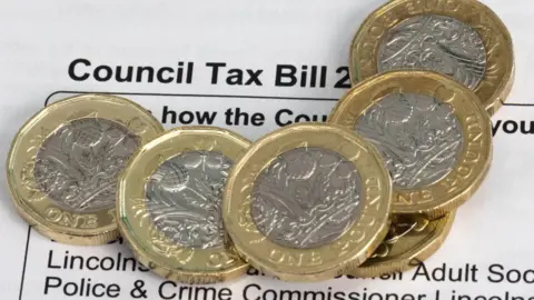 A close-up photo of a council tax bill with several £1 coins stacked on top.