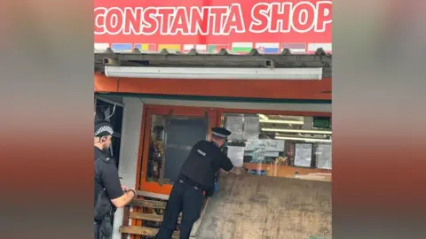 Cambridgeshire Constabulary Police officers placing a notice on the Constanta Shop window