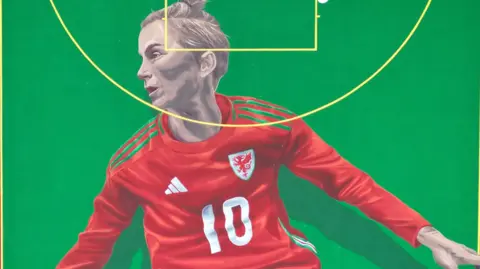 A mural of Jess Fishlock, wearing the Wales number 10 shirt, against a green backdrop