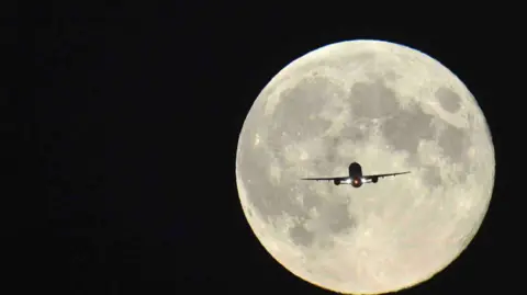 Reuters A plane is silhouetted by a full Moon and a dark black night sky