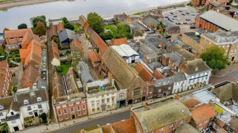 George's Guildhall Charity Aerial view of the George’s Guildhall. There are other buildings in the aerial photo. There is water in the background at the top of the frame.