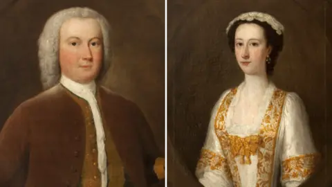 National Trust A painted image of Thomas Ferrers and his wife, Margaret. He is wearing a grey wig, white shirt and burgundy jackets. She is depicted in a white dress with gold trim around the neck, chest and sleeves. 