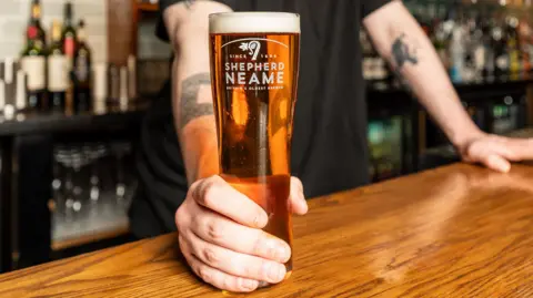 A pint of beer in a Shepherd Neame glass with a man holding it.