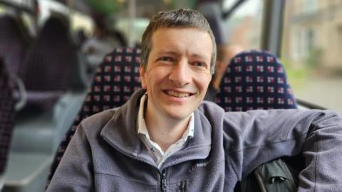 Smiling man in a fleecy top riding a bus