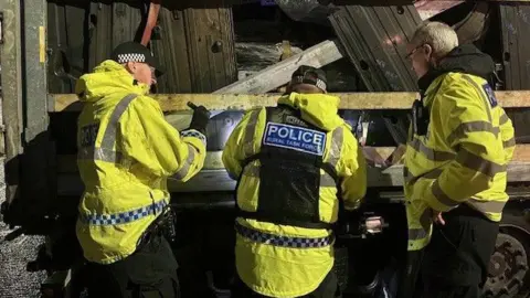 Three officers in uniform are checking a lorry that's leaving the UK loaded with vehicle parts