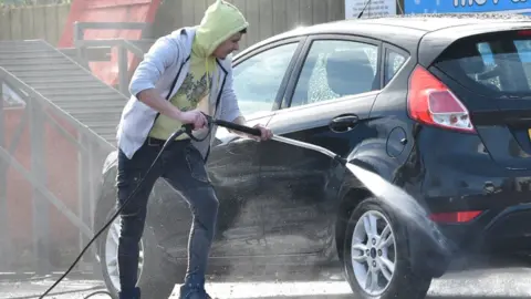 Pacemaker A man in a yellow hooded top using a power hose to clean a car