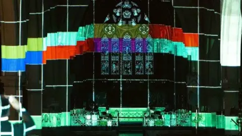 The main stained glass window of the church with horizontal bands of colour projected onto it