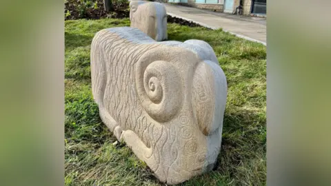 A stone sheep. It is a cuboid shape with rounded edges. It has curled horns on the side.