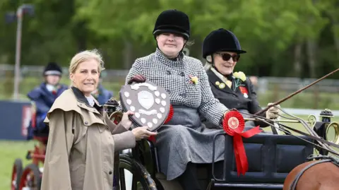Princess Sophie can be seen giving Rebecca Stevens a shield. They are both in formal wear on the grounds of at Royal Windsor Horse Show.