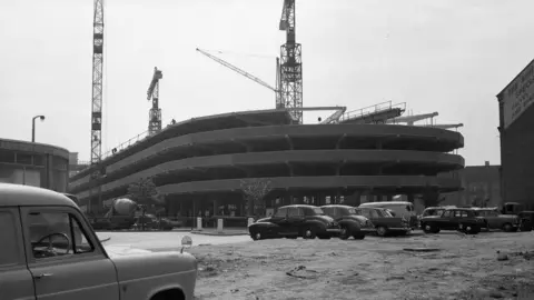 Leicester Museums and Galleries A black-and-white photo of cranes on top of a semi-completed car park building 