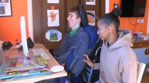 BBC William and his carer looking at a computer screen at a desk