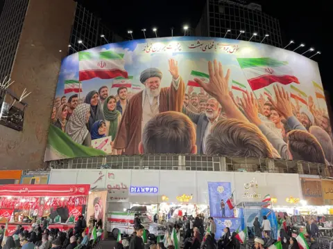 A large mural depicting the late ayatollah hangs over a busy shopping street