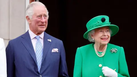 Getty Images King Charles III with his late mother, Queen Elizabeth II - both are smiling off camera, and standing on the Buckingham Palace balcony which can just be seen. The late Queen wears an emerald green hat and jacket, with pearls and a diamond brooch in the shape of a bow, while the King has a navy pin-striped suit and a pale blue patterned tie 