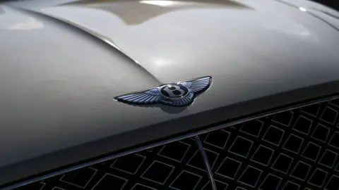 PA Media The Bentley logo on the front of a grey car, just above the radiator grill. The badge is a central "B" with wings either side.