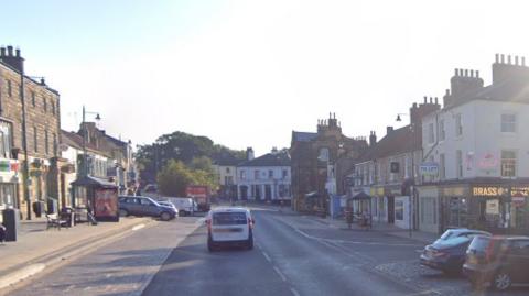 Guisborough high street, lined with businesses and parked cars to either side of the high street.