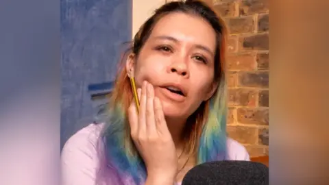 Ria Lina holds her chin while thinking