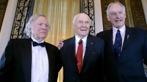 AFP via Getty Images Three men in business suits smile with their arms around each other 