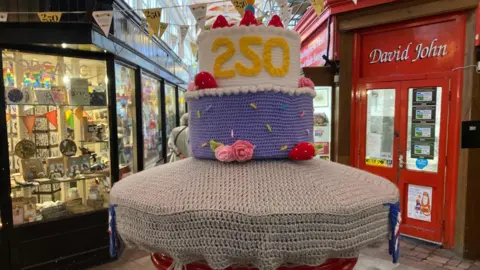 Oxford City Council The postbox in the market covered in crocheted yarn in the shape of a 250th birthday cake.