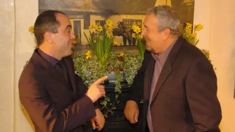 Pacemaker Press Gerry Kelly and Jimmy Nesbitt talking while both wearing grey blazers and purple coloured shirts.