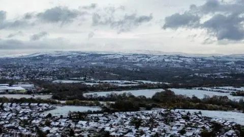 Sunset Twilight/BBC Weather Watchers Snow-covered panorama with houses and trees in the foreground and hills in the background