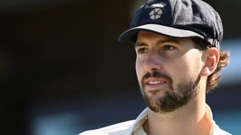 Ben Aitchison looks on wearing a blue Derbyshire cap