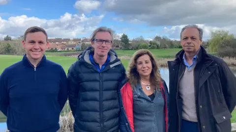 Three men and one woman are posed standing on a golf course.