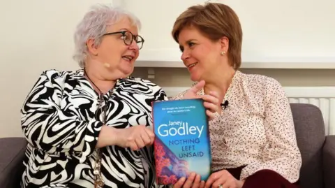 Los periodistas de PA, Janey Godley y Nicola Sturgeon, sostienen una copia del libro de la Sra. Godley. 