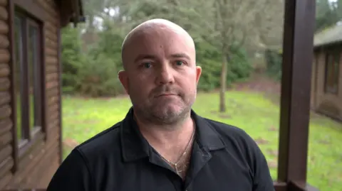 BBC Harvey Cooper wearing a dark t-shirt standing in front of grass and trees