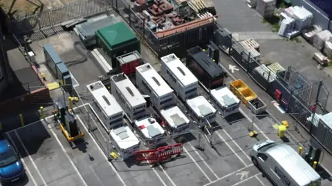 An aerial view of the generators in a car park. They look like large, white shipping containers.