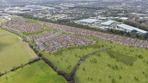 CGI image of overhead shot looking at green fields. A large portion of these fields are taken by rows of houses. 