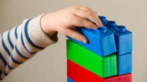 A closeup of a child's hand on some toy bricks stacked up on top of each other. 