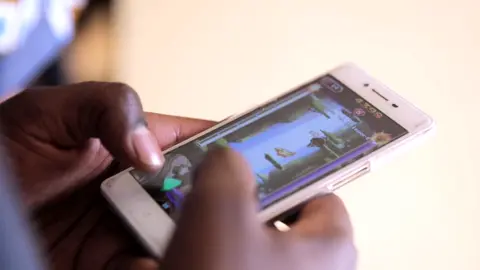 BBC A man playing the Mzito mobile game