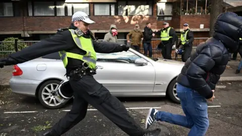 Getty Images A police officer chases a man through streets close to the 'National March For Palestine' in central London on November 11, 2023, as counter-protest groups are monitored by police close to the route of the main march