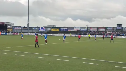 Footballers play on a pitch in red and blue kit.